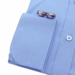 Detalhe do punho duplo rígido da camisa azul clara lisa italiana com abotoaduras metálicas em destaque sobre o tecido sulfite.