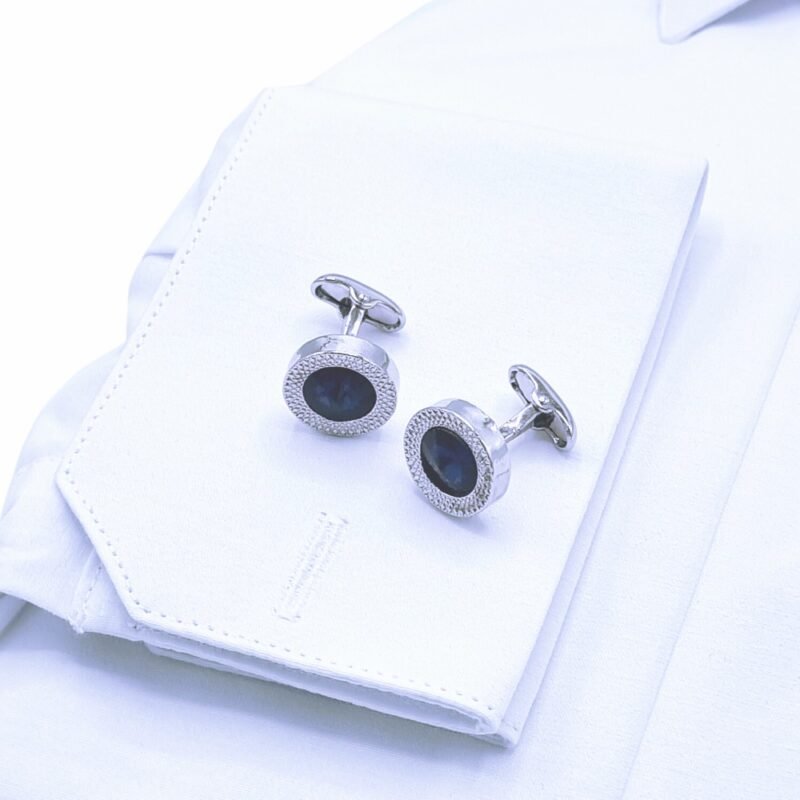 Close do punho duplo rígido da camisa italiana branca lisa com abotoaduras escuras em destaque.