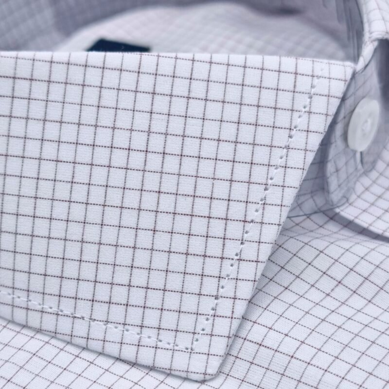 Close da textura do tecido quadriculado branco e bordô da camisa italiana fio egípcio, mostrando a trama discreta e o caimento suave na região da gola.