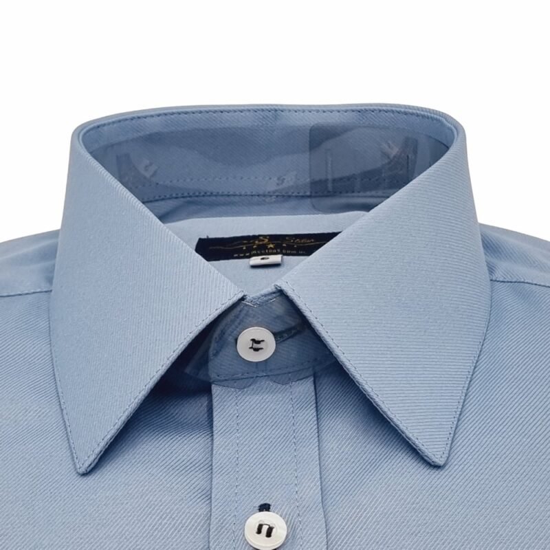 Close frontal da gola francesa da camisa social azul maquinetado, destacando colarinho rígido e acabamento das costuras.
