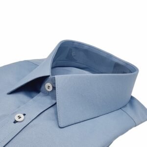 Close lateral da gola francesa da camisa azul maquinetado com punho duplo, evidenciando a estrutura do colarinho e a textura do tecido.