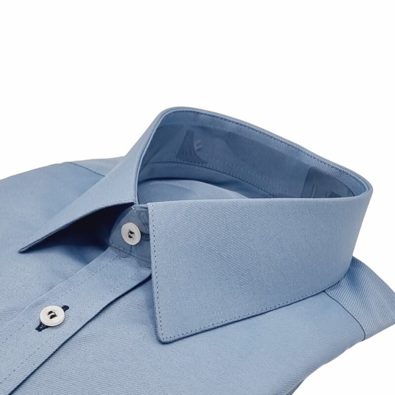 Close lateral da gola francesa da camisa azul maquinetado com punho duplo, evidenciando a estrutura do colarinho e a textura do tecido.