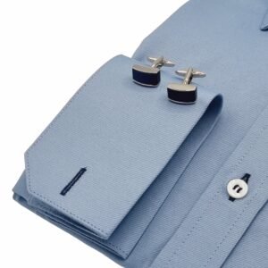Detalhe do punho duplo da camisa azul maquinetado francesa com par de abotoaduras metálicas em destaque.