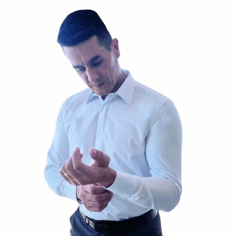 Modelo usando camisa francesa branca lisa sulfite enquanto ajusta o punho, reforçando a ideia de preparação cuidadosa para um compromisso importante.