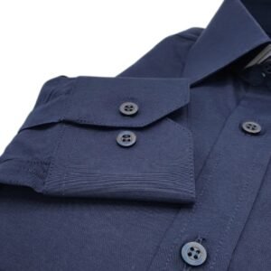 Close do punho com botões da camisa social azul marinho lisa francesa, destacando costuras, textura do tecido e acabamento do punho.