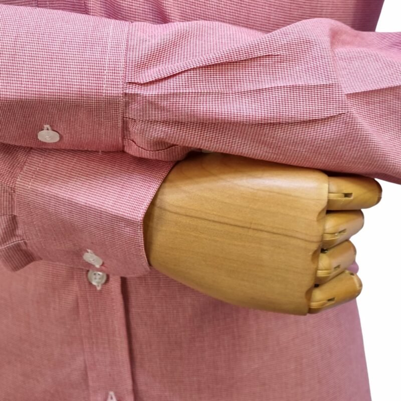 Close no punho com botão e manga cruzada da camisa social vermelha 100% algodão sobre mão de manequim de madeira.