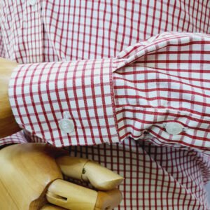 Close no punho com botão da camisa xadrez vermelho em algodão passa fácil apoiado na mão de manequim de madeira.