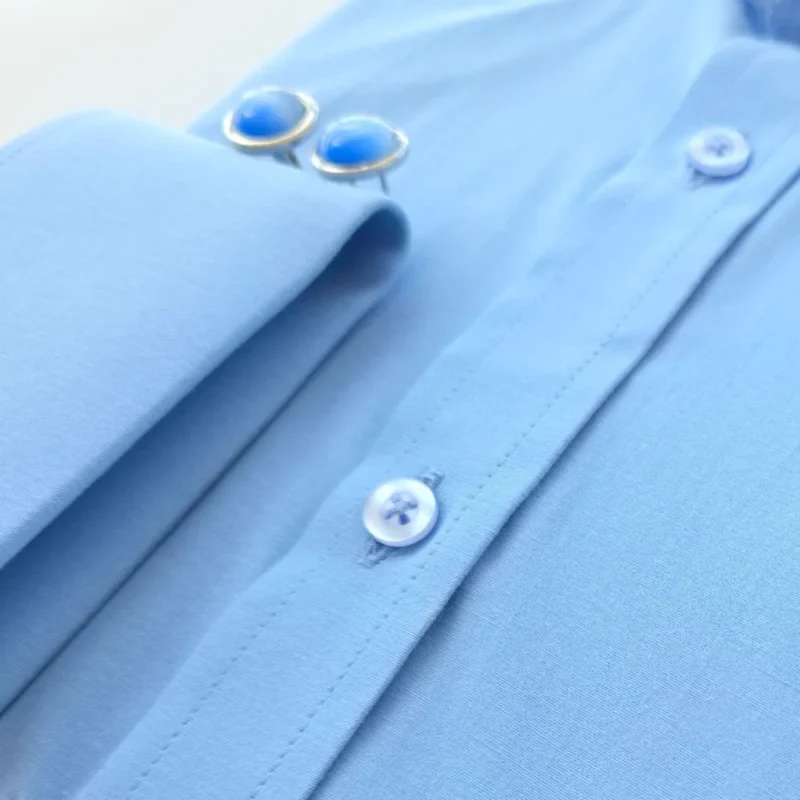 Detalhe do punho duplo dobrado da camisa azul lisa, com a barra de botões ao lado