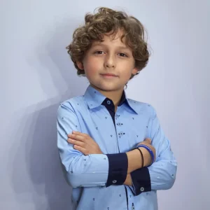 Menino de braços cruzados com a camisa kids azul de âncoras e o punho marinho dobrado