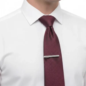 Prendedor de gravata prata preso à gravata bordô sobre camisa social branca
