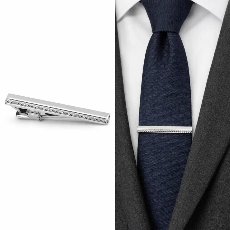 Prendedor de gravata prata em close e preso na gravata azul marinho com camisa branca