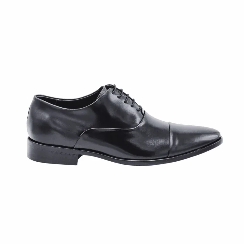 Perfil lateral do sapato social Oxford preto, com o bico alongado e o salto de couro