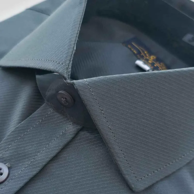 Colarinho fechado no botão superior da camisa cinza chumbo, com a textura em linhas diagonais
