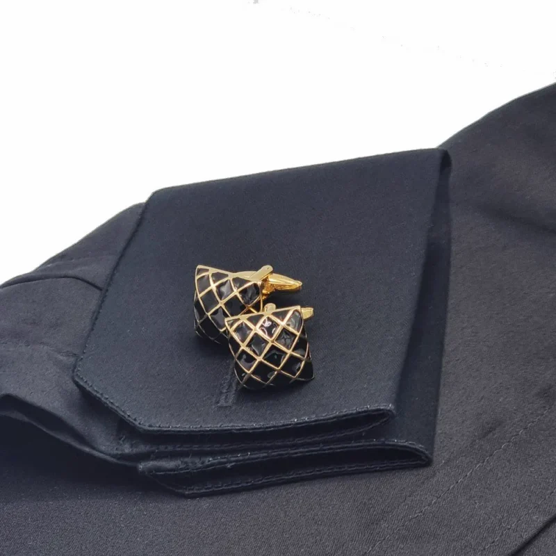 Punho duplo da camisa preta com o par de abotoaduras douradas quadriculadas